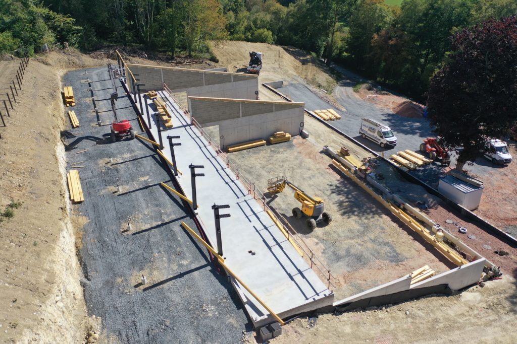 Vue aĂ©rienne dâun chai viticole en construction par Constructions BOULAY, au cĆur dâun vignoble en Normandie, avec les murs bĂ©ton et la charpente en cours de montage.