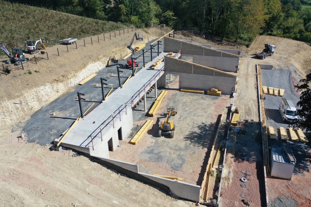 Vue aĂ©rienne dâun chai viticole en construction par Constructions BOULAY, au cĆur dâun vignoble en Normandie, avec les murs bĂ©ton et la charpente en cours de montage.