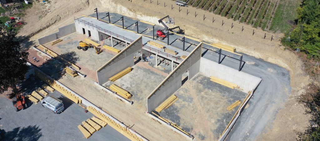 Vue aĂ©rienne dâun chai viticole en construction par Constructions BOULAY, au cĆur dâun vignoble en Normandie, avec les murs bĂ©ton et la charpente en cours de montage.