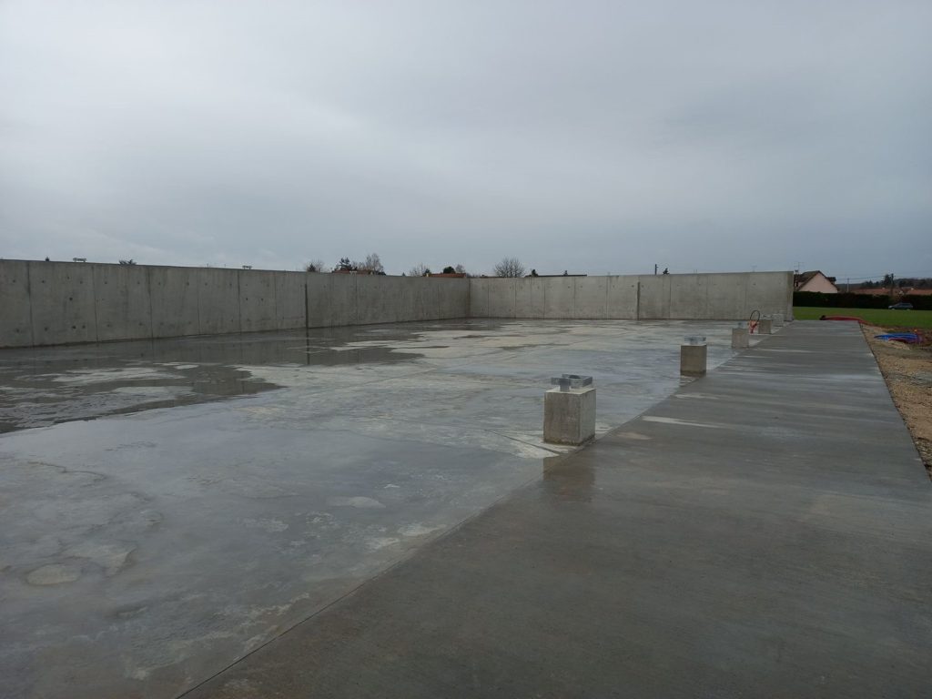 Dallage en béton et murs en béton armé réalisés par les Constructions Boulay pour un bâtiment de stockage agricole en Normandie, avec dés béton pour l'ancrage de la charpente.