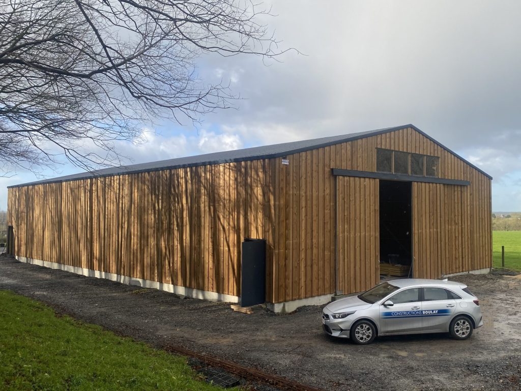 Bâtiment agricole à bardage bois vertical avec grande porte coulissante et soubassement béton – Constructions Boulay.