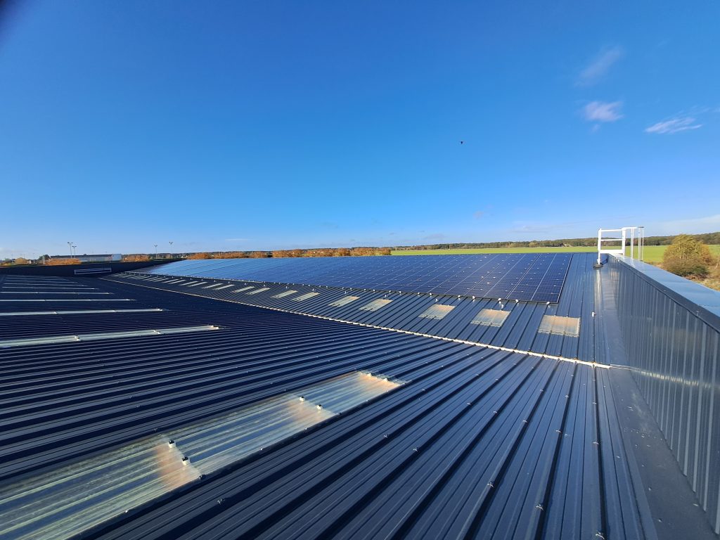 Couverture de bâtiment industriel en panneaux sandwich isolants en acier, intégrant des panneaux photovoltaïques et des plaques translucides pour l'éclairage naturel, réalisée par Constructions Boulay en Normandie.
