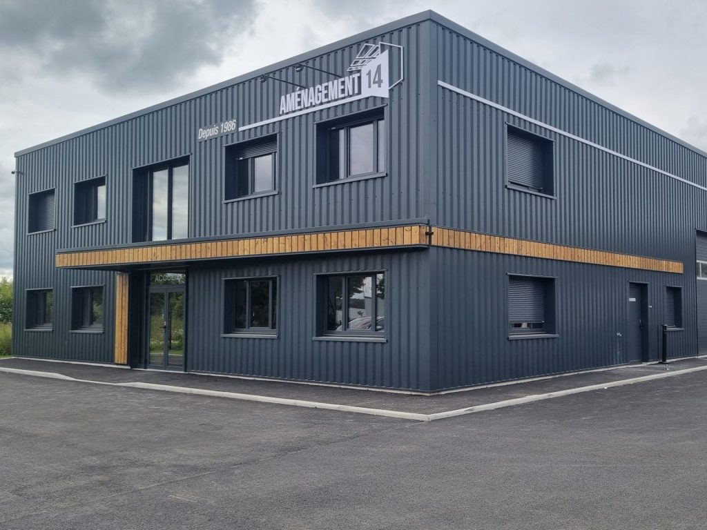 Bardage métallique vertical gris anthracite sur bâtiment industriel à deux niveaux, avec bande décorative en bois – Constructions Boulay