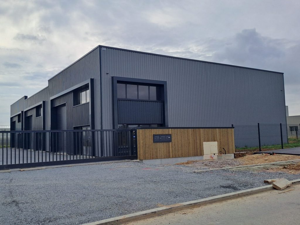 Bâtiment d'activités revêtu de bardage acier gris clair et anthracite, avec volumes de façade et vitrages – Constructions Boulay.